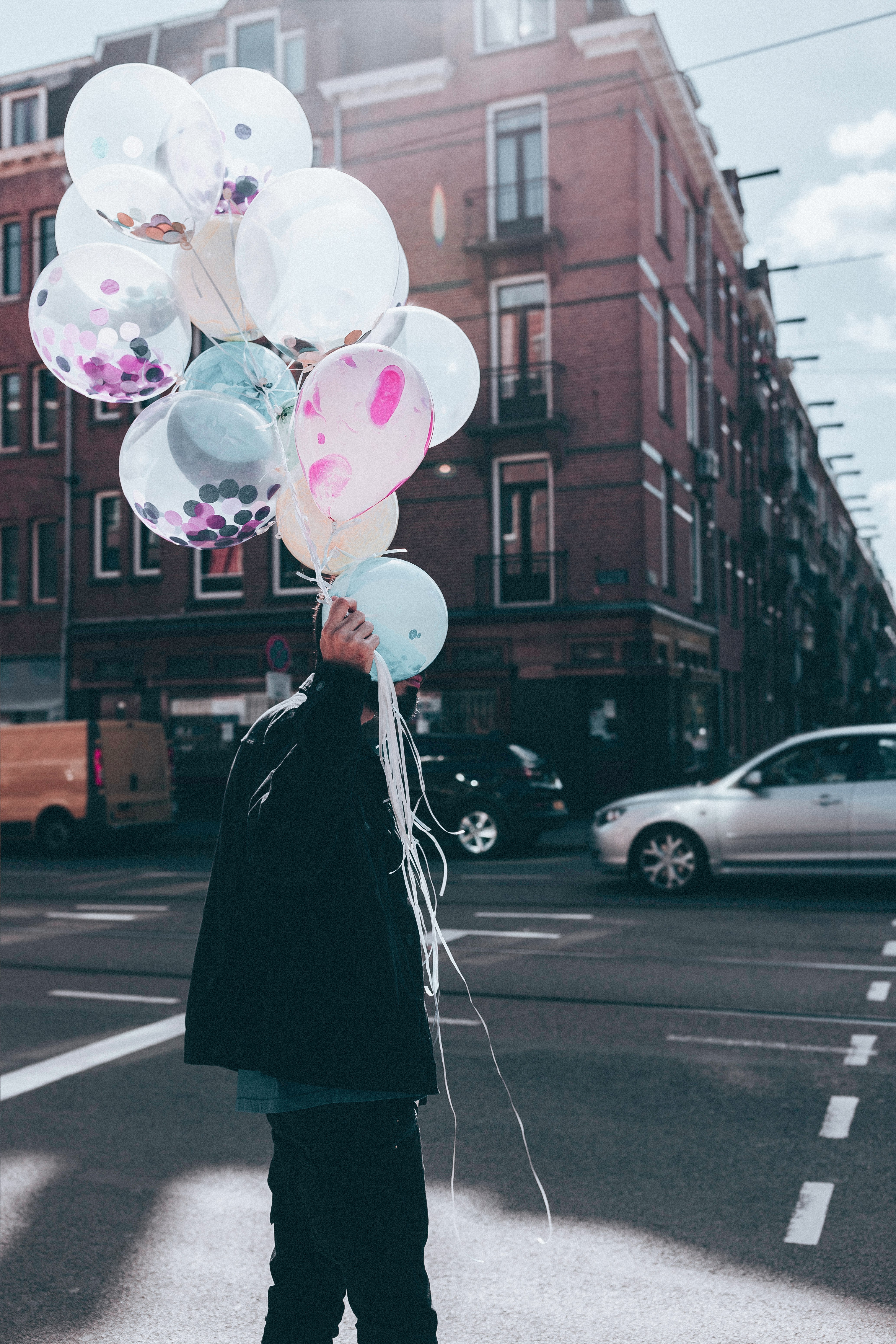 man holding white balloon walking on street during day time